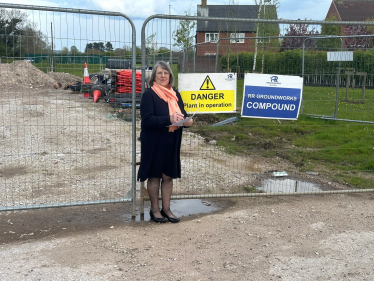 Fiona Bruce MP standing in front of harris fencing on a building site